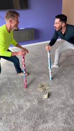 two men in a living room playing with baseball bats and money on the floor next to each other