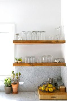 two wooden shelves filled with glasses and lemons on top of a marble countertop