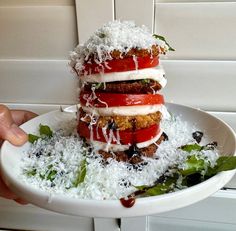 a stack of food sitting on top of a white plate covered in shredded parmesan