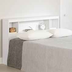 a white bed with two pillows on top of it and an alarm clock above the headboard