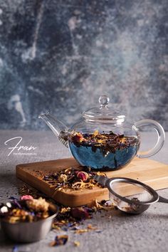 a glass teapot filled with flowers next to a wooden cutting board and measuring spoon