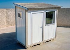 a small white storage shed sitting on top of a cement floor next to a wall