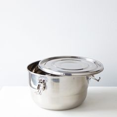 two stainless steel pots sitting side by side on a white counter top, one has a lid and the other is empty