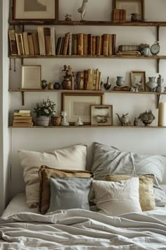 a bed topped with lots of pillows next to shelves filled with books and vases