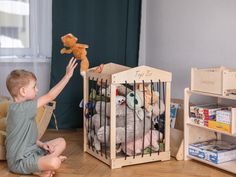 a little boy sitting on the floor in front of a crib with stuffed animals