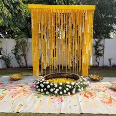 a decorated stage with yellow curtains and flowers on the ground, in front of a white fence