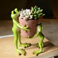 two green frog figurines holding a potted plant on top of a book