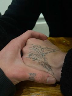 two people are holding hands with tattoos on their palms and fingers, while the other hand has a cross tattooed on it