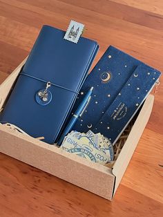 a blue notebook and pen in a box on a wooden floor with other items inside