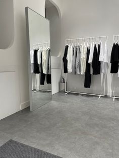 an empty room with clothes hanging on racks and a large mirror in the corner next to it