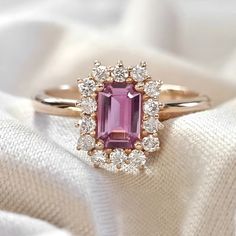 a pink tourmaline and diamond ring sitting on top of a white cloth