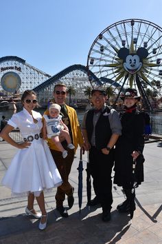 three adults and two children posing for a photo in front of mickey mouse's amusement park