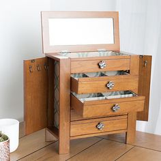 a wooden jewelry box with three drawers and a mirror on the top, sitting on a wood floor