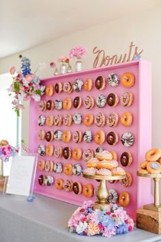 a table topped with lots of donuts on top of a pink tray next to a sign