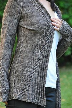 a woman standing in the grass wearing a cardigan