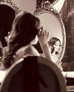 a woman sitting in front of a mirror brushing her hair