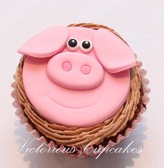 a pink cupcake with a pig face on it's side sitting in a wicker basket