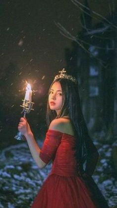 a woman in a red dress holding a candle and wearing a tiara with snow falling around her