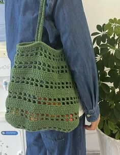 a person holding a green crocheted bag in front of a potted plant