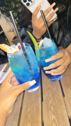 two people sitting at a table with blue drinks in front of them and one holding a cell phone