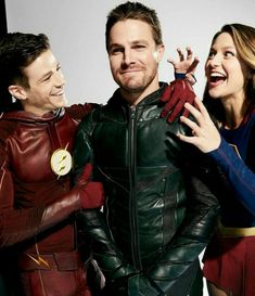 the flash and supergirls are posing for a photo in their costume outfits, with one man holding his arm around the woman's shoulder