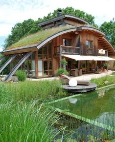 an unusual house with a green roof on the water's edge is surrounded by tall grass