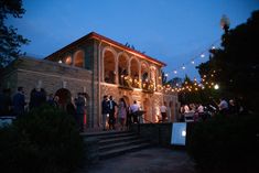 a group of people standing in front of a building with lights strung from the roof