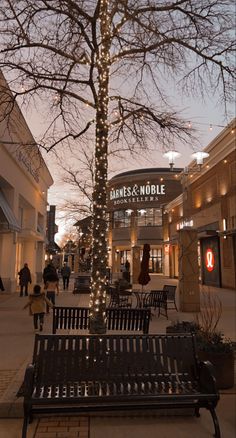 a bench sitting in the middle of a sidewalk next to a tree with lights on it