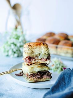 two sandwiches stacked on top of each other on a white plate with goldware next to them