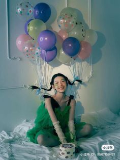 a woman in a green dress sitting on a bed with balloons above her head and smiling at the camera