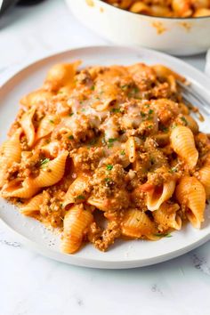 a white plate topped with pasta covered in meat and sauce next to a casserole dish