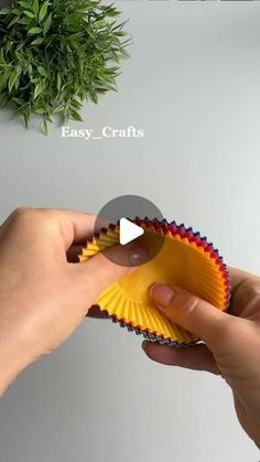 someone is holding a paper cupcake liner in front of a green potted plant