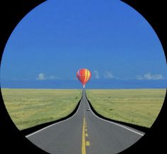 an image of a hot air balloon flying in the sky over a road with grass