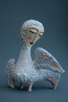 a ceramic sculpture of a woman with wings on her head and body, sitting in front of a gray background