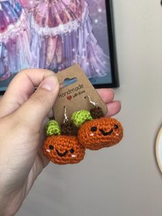 a hand holding two small crocheted carrots in front of a card board