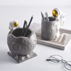 a pair of glasses sitting on top of a desk next to a cup filled with pens and pencils