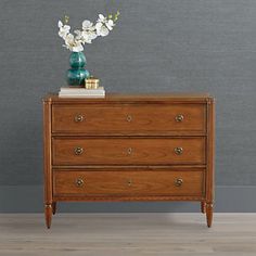 a wooden dresser with flowers on top and a vase sitting on top of the drawers