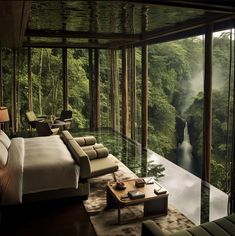 a bedroom with a large glass wall overlooking the water and trees in the forest is shown