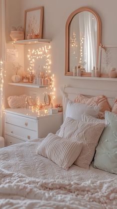 a white bed topped with lots of pillows next to a mirror and lights on the wall