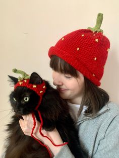 a woman holding a black cat wearing a strawberry hat