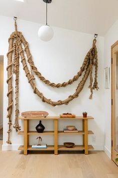 a room with a table, shelf and hanging decorations on the wall above it is an entry way that has been decorated with jute rope