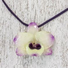 A real Dendrobium Orchid preserved in resin is showcased in this pendant necklace presented by Danai of Thailand. The orchid has pale yellow petals tipped in purple and hangs from a deep purple leather cord. Two sliding tiger's eye beads dyed purple secure the ends of the cord and allow the necklace length to be adjusted. Dendrobium Orchid, Gifts For Travelers, Orchid Necklace, Yellow Petals, The Orchid, Yellow And Purple, Purple Orchids, Dope Jewelry, Flower Pendant Necklace