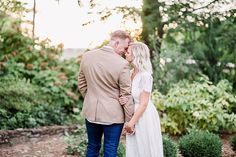 a man and woman standing next to each other in front of some bushes with trees