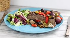 a blue plate topped with meat and veggies next to a knife and fork