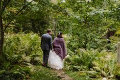 a bride and groom walking through the woods