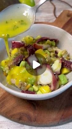 a white bowl filled with vegetables and dressing being poured into it on top of a wooden cutting board