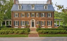 a large brick house with blue roof and shuttered windows on the front, surrounded by hedges