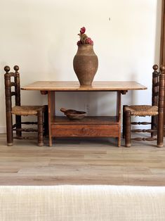 a wooden table with two chairs and a vase on top