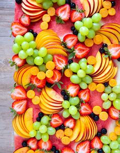 an arrangement of fruit arranged on top of a watermelon and grape tray with blackberries, oranges, grapes, and strawberries