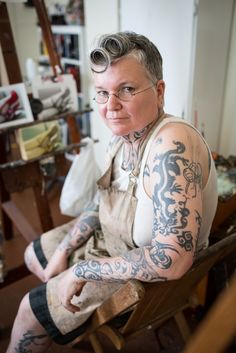 a tattooed man sitting in a chair with glasses on his head and tattoos on his body